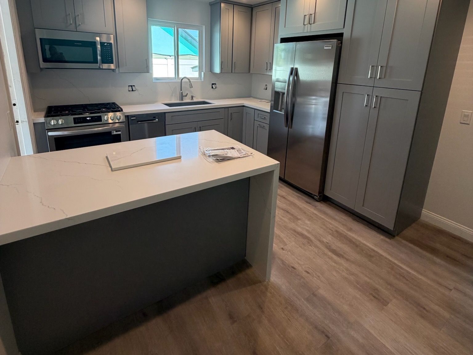 Remodelled kitchen with grey shaker cabinetry, a veined quartz island, stainless gas range and refrigerator, and luxury vinyl plank flooring